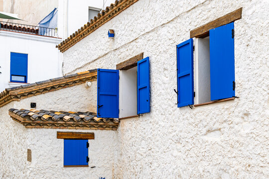 Traditional Mediterranean house with white stucco walls, wooden accents, and blue wooden shutters on open windows. Rustic European architecture in a coastal village.