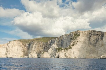 Coastal cliffs rise majestically above calm waters under a partly cloudy sky, embodying the beauty...