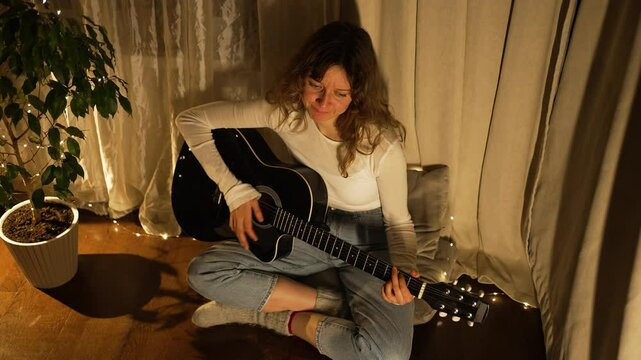 Soft warm lighting enveloping young woman practicing acoustic guitar, creating serene musical atmosphere within intimate living room setting