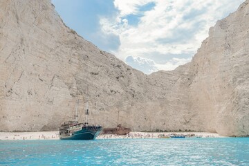 Visitors enjoy the beautiful sandy beach of Navagio surrounded by towering cliffs. Bright blue...