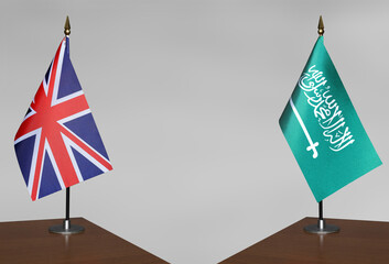 Tabletop flags of United Kingdom and Saudi Arabia on stands on a gray blurred background