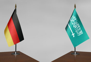 Tabletop flags of Germany and Saudi Arabia on stands on a gray blurred background