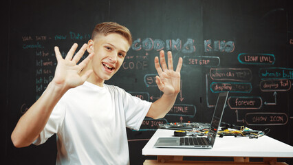 Side view of young boy programing code while looking at camera and greeting. Highschool student...