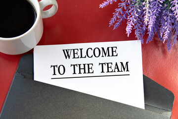 WELCOME TO THE TEAM - the words on white paper are on a black envelope on a red background.