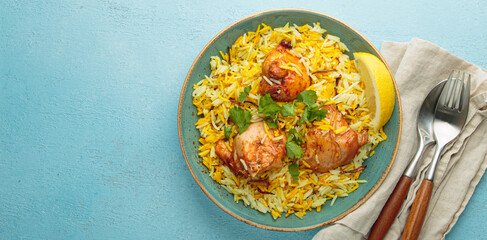 Delicious indian chicken biryani with chicken, garnished with fresh cilantro and lemon, in a bowl on a blue table with copy space. Authentic dish of India