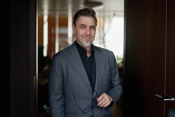 Business portrait - confident businessman standing in office. Happy mid adult man in shirt and...