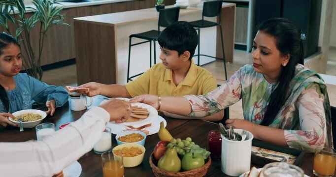 Indian Asian young family of four, including loving parents, son, a daughter, joyfully having breakfast together at a dining table in a beautifully designed modern home, enjoying a healthy meal