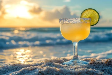 Gardinen Refreshing margarita cocktail stands on a sandy beach as the sun sets over the ocean, creating a tranquil and inviting scene © Michael