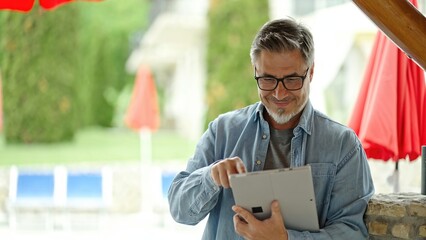 Middle age man talking on video call with tablet computer outdoor in garden, happy, smiling. Home...