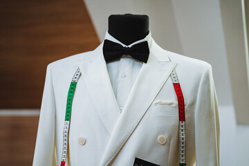 A stylish white suit with a classic black bow tie is elegantly displayed on a mannequin, showcasing...