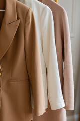 sleeves of three womens blazers in light neutral colors hanging from a gold rack