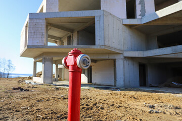 A red hydrant with water against the background of an unfinished apartment building.