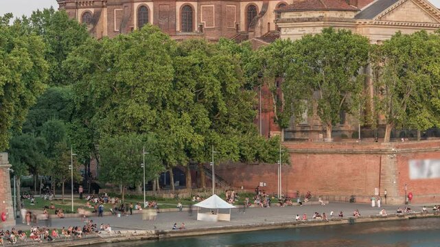 Aerial view of Port de la Daurade park along the Garonne River timelapse in Toulouse, France. Sunset orange light, ferry at the dock and people enjoying the vibrant riverside atmosphere