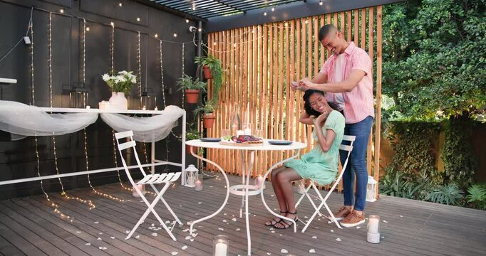 Romantic dinner on patio, diverse couple enjoying candlelit evening with flowers and lights