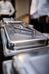 Catering setup with metal food trays and serving utensils in a restaurant environment during an event