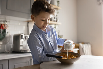 Cute little boy standing in modern kitchen in morning preparing independently breakfast before...