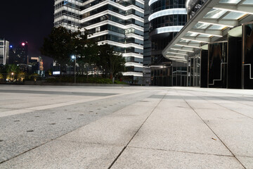 empty ground of modern street with illuminated office buildings at night.