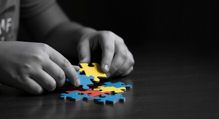 Child's hands assembling colorful puzzle pieces on dark table. Close-up of fingers connecting blue and yellow jigsaw parts. Problem-solving, cognitive development. autism awareness