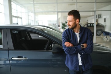 Handsome bearded buyer in casual wear in dealership, guy standing near car