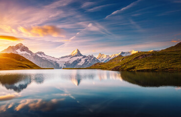 A high snow-capped rocky massif is reflected in Lake Bachalpsee at sunset. Location place Bernese Alps, Grindelwald valley, Europe.