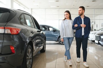 It is the one car I want. Beautiful young couple standing at the dealership choosing the car to buy
