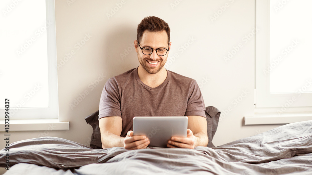 Leinwandbilder man using digital tablet watching movie online sitting in bed in bedroom at home on weekend. guy rel