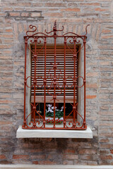 The brick wall with a window featuring metal grillwork and flowers in jars. These flowers create a sense of comfort and look amazing against the background of the dark brick wall
