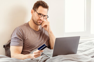 Concerned Man Holding Credit Card Shopping Online On Laptop Having No Money At Home. Online Payment, Bank Account Problem.
