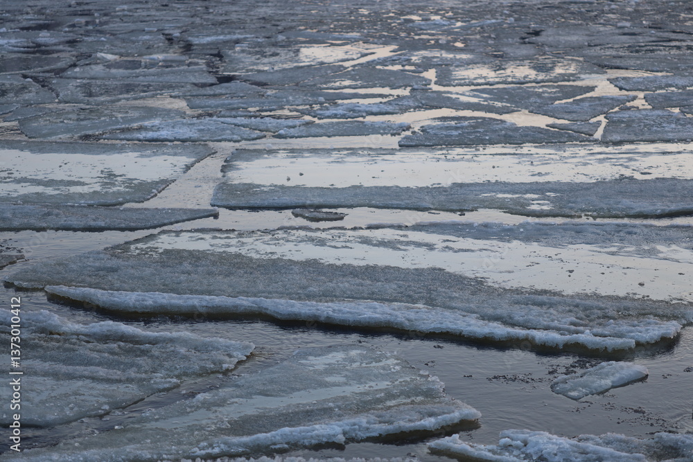 Poster pieces of ice floating on the surface of a river, potentially melting or already broken apart.