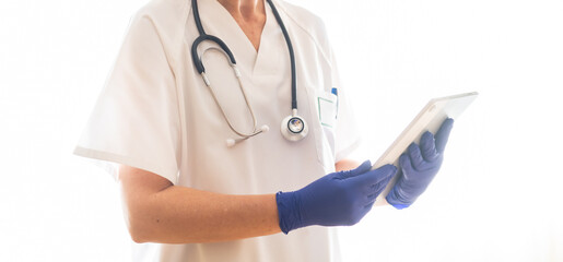 Medical professional wearing blue gloves and a stethoscope consults a tablet, likely reviewing...