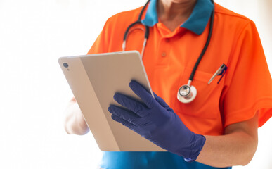 Paramedic in blue gloves and an orange-blue uniform using a digital tablet, with a stethoscope around the neck, highlighting technology's role in healthcare