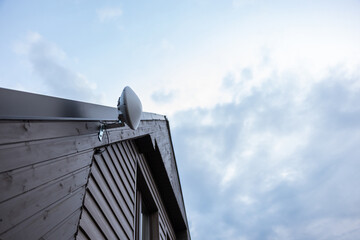 Corner of a wooden house with slanted roof, featuring a white dome shaped Wi Fi router on a metal...