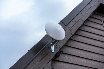 White circular Wi Fi router attached to wooden siding near roofline of private house with slanted...