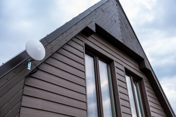 Upper section of a modern house with dark wooden siding, large vertical windows, and a white circular Wi Fi router mounted near the roofline.