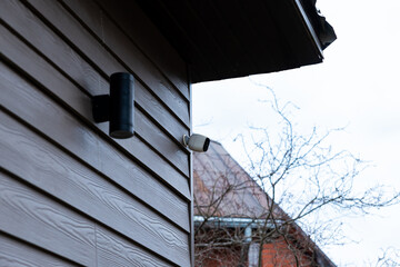 Exterior of a house with wooden siding, a security camera near the roofline, and a black outdoor...