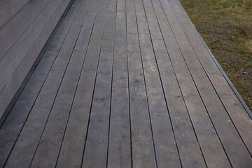 Wooden deck with evenly spaced planks next to a house with horizontal siding. The deck transitions...