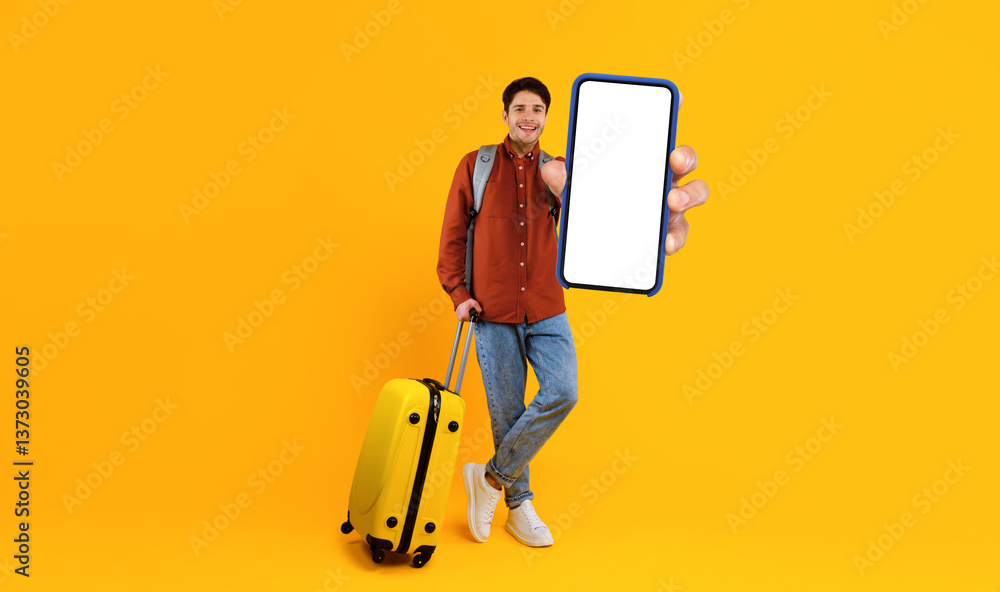 Poster male tourist showing smartphone empty screen holding big phone in hand standing with suitcase smilin