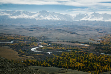 A panoramic view of a golden autumn forest with winding rivers and snowy mountains on the horizon...