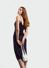 Fototapeta premium A beautiful stylish woman with long well-groomed hair in a silk dress poses holding a fashionable white bag in her hands. The image of spring-summer 2025