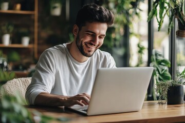 A young man happily reads a laptop at home relaxed at a wooden table while practicing soc