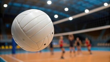 Close-up of a white volleyball in mid-air with players in the background of an indoor court