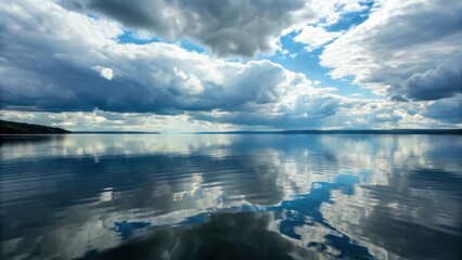Obraz premium Cloudy sky reflecting on a calm lake surface with a distant horizon
