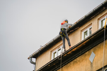 Rope access technician in harness and helmet performs maintenance on building exterior, working at height