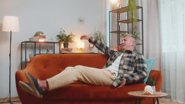 Tired young man with gray hair sitting on comfortable couch, taking a rest, daytime nap. Portrait of carefree Caucasian guy relaxing, resting, falling asleep at home apartment in living room on sofa