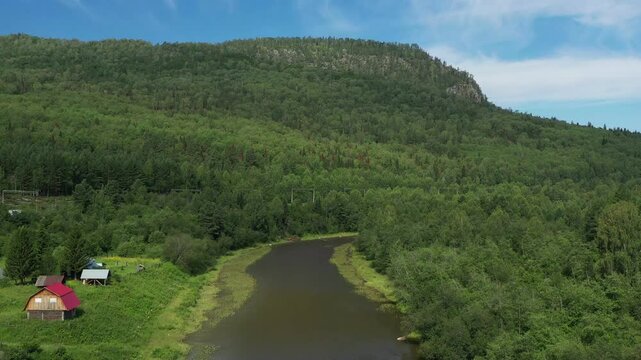 Ural mountains. Aygir village. Camera slowly moving upwards, showing a river running through a forest next to a farm and a mountain