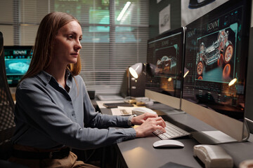 Young serious businesswoman looking at computer screen while creating 3d graphic model of new car...