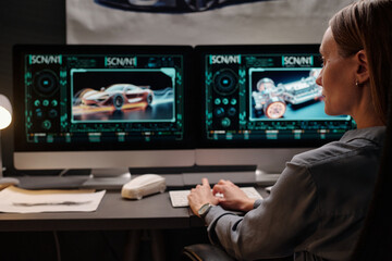 Young female engineer sitting in front of computer monitors and working over new graphic models of automotive vehicles