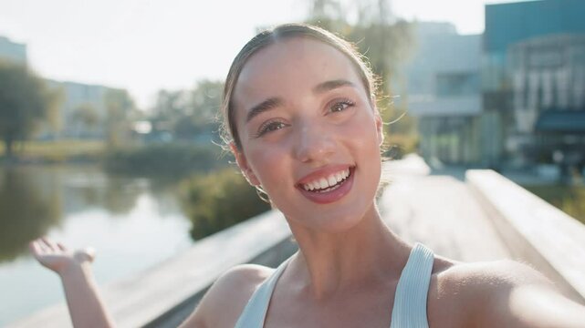 Close-up POV of young athlete woman talking on video call in urban city park. waving and looking at camera happy sporty girl shares updates on training and upcoming competitions enthusiasm and energy.