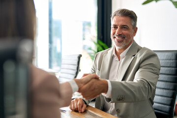 Happy mature business man bank manager or lawyer handshaking client at office meeting. Smiling...