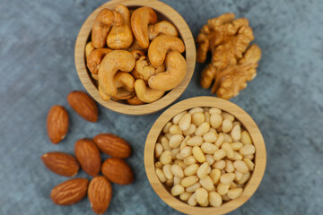 Close-up view from above of wooden bowls with pine nuts and cashews, which stand on the side surrounded by walnuts and almonds on a gray background. The concept of healthy snacks, healthy and